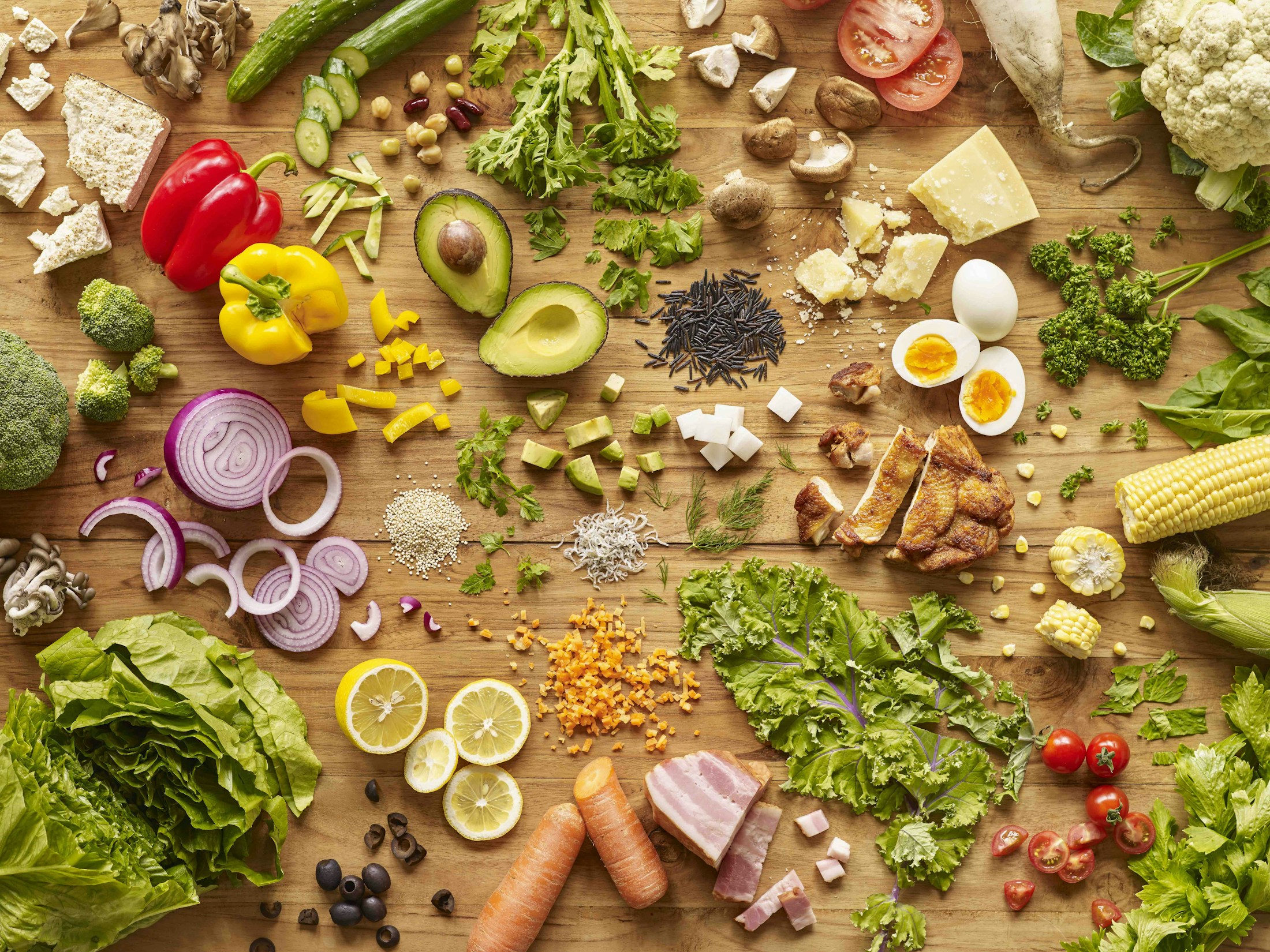 Vegetables, avocado, grains, eggs and other ingredients arranged on a wooden table